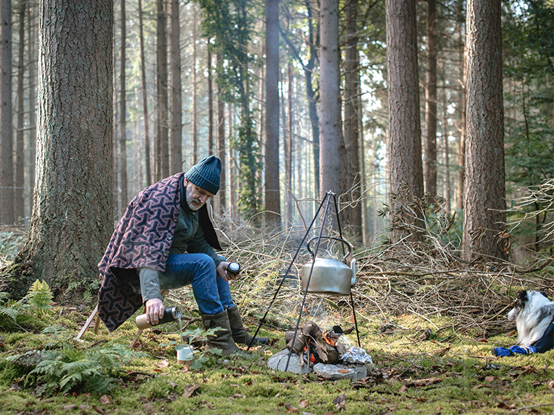 Mann mit Geschenktipp Wärmedecke im Wald sitzend