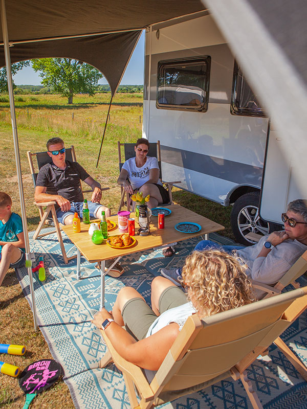 Familie mit Wohnwagen mit schwarzem Sonnensegel, Outdoor-Matte ausgebreitet